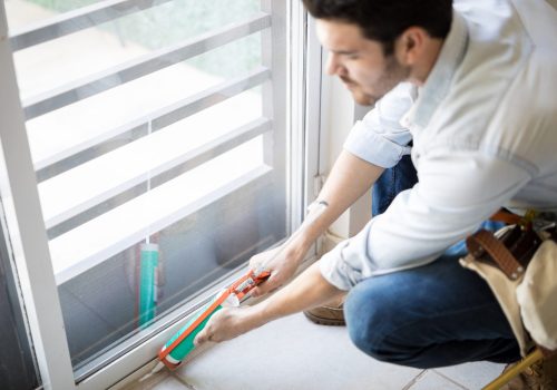 Closeup of a young handyman applying some sealant on a door with a sealing gun